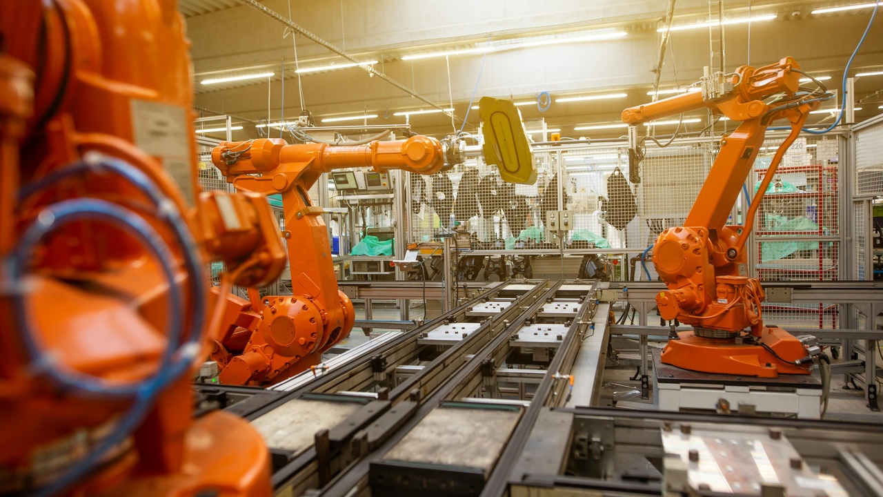 Factory floor with robotic arms and human workers, illustrating automation's impact on jobs.