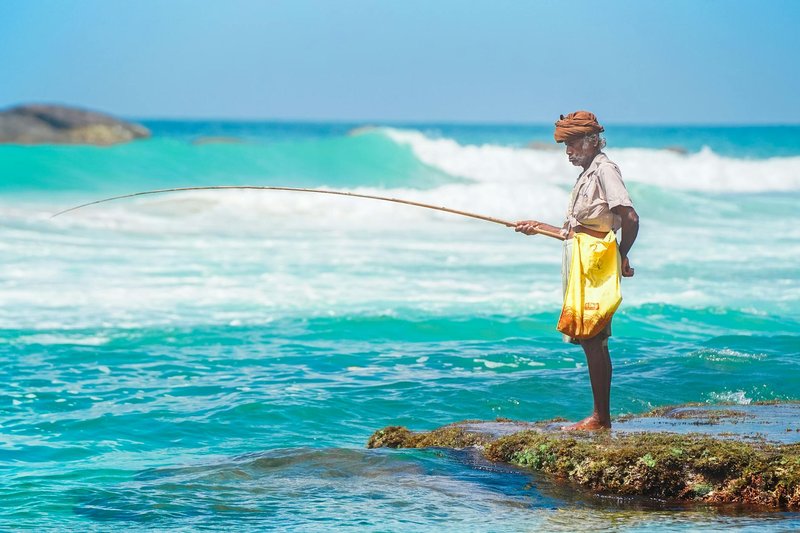 Senior man fishing on a rocky coast with waves crashing, embodying serene coastal lifestyle.
