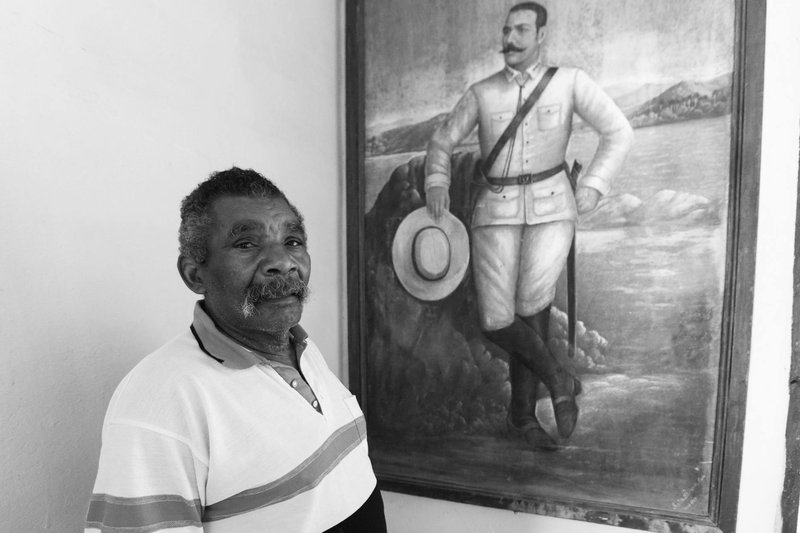 Black and white portrait of a man beside a historical painting, showcasing cultural heritage.