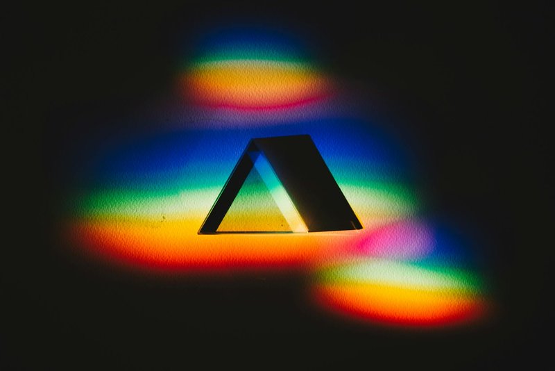 Colorful dispersion of light through a prism creating a vibrant rainbow spectrum on a dark background.