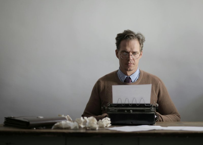 A thoughtful male writer typing on a vintage typewriter, surrounded by crumpled papers.