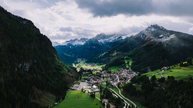 Scenic aerial view of Canazei in Trentino-Alto Adige, surrounded by lush valleys and majestic mountains.
