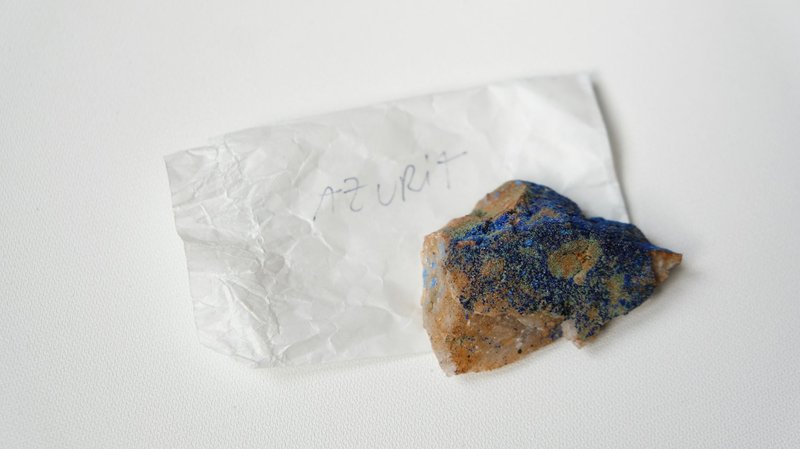 From above of multicolored stone Azurite placed on small sheet of paper with inscription on  white table
