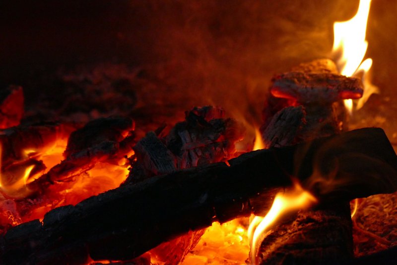 Warm, glowing embers of a campfire with dancing flames and charred wood, creating a cozy atmosphere.