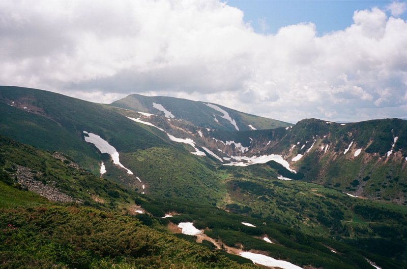 Breathtaking view of lush green mountains with snow patches under a cloudy sky.