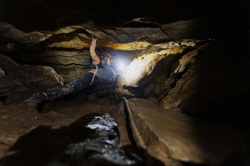 Dynamic image of a caver navigating a rocky subterranean world with headlamp illumination.