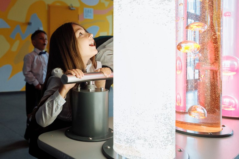 Children engage with interactive science exhibit featuring colorful liquids and lights.