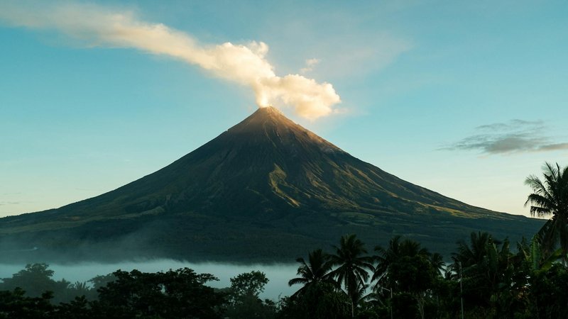 Stunning view of Mayon Volcano emitting smoke surrounded by lush tropical landscape in the Philippines.
