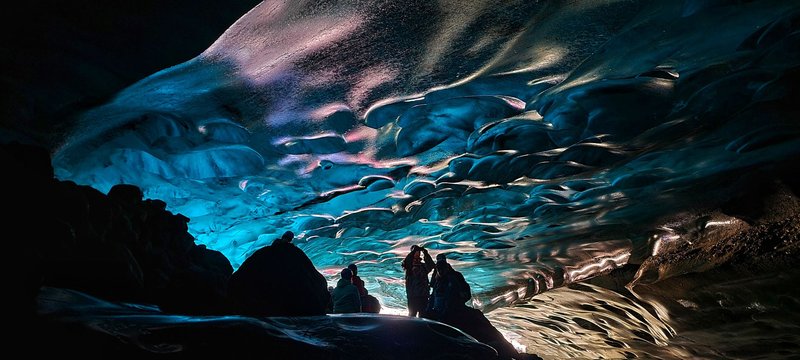 A mesmerizing view of people exploring a dazzling ice cave with ethereal lighting.