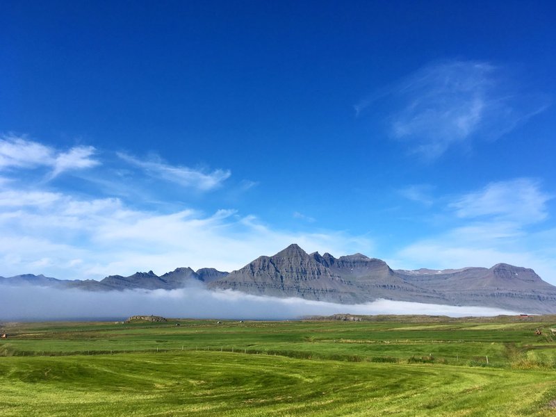 Stunning view of rocky mountains in Iceland with lush fields under a bright blue sky.