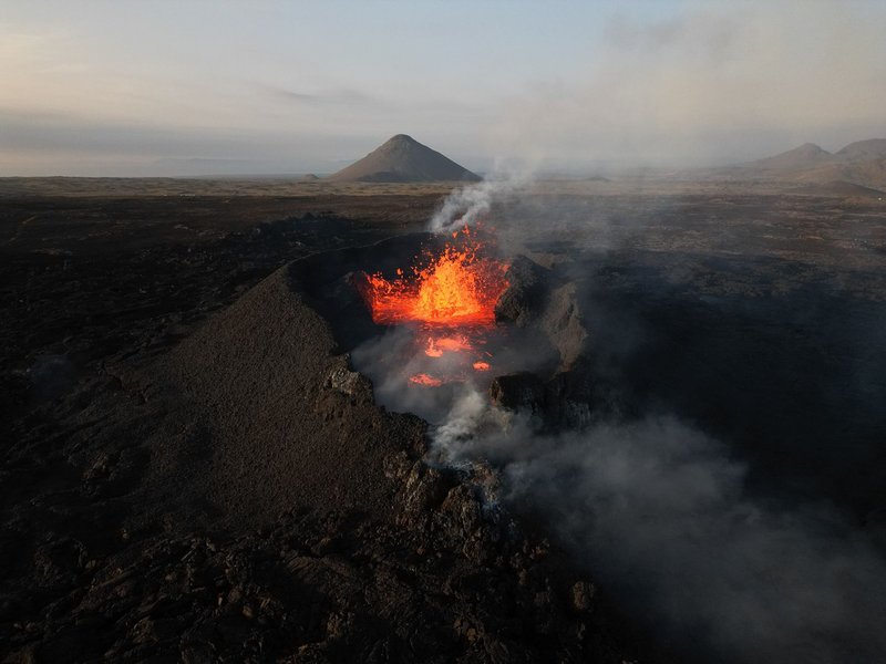 An erupting volcano in Iceland captured from above, showcasing vibrant lava and smoke.
