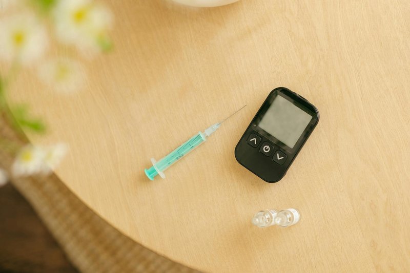 Close-up of a glucometer, syringe, and vials on a wooden table for diabetes care.