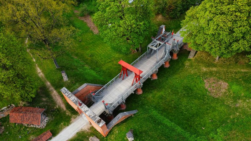 An aerial shot of the historic wooden drawbridge at Biržai Castle, surrounded by lush greenery in Lithuania.