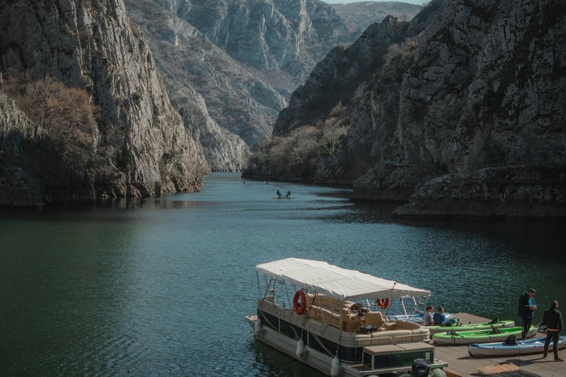 Stunning view of Matka Canyon with a boat and kayaks surrounded by towering cliffs.