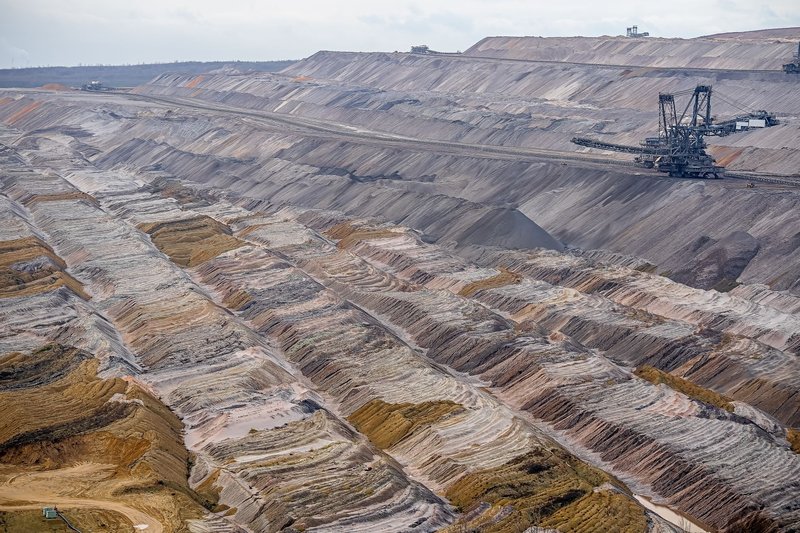 Aerial view of a large, barren open-pit mine featuring machinery and textured soil layers.