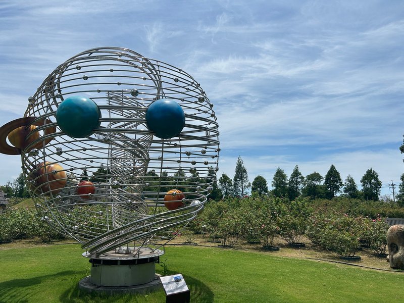Intricate metallic sculpture of the solar system in a lush outdoor garden setting.