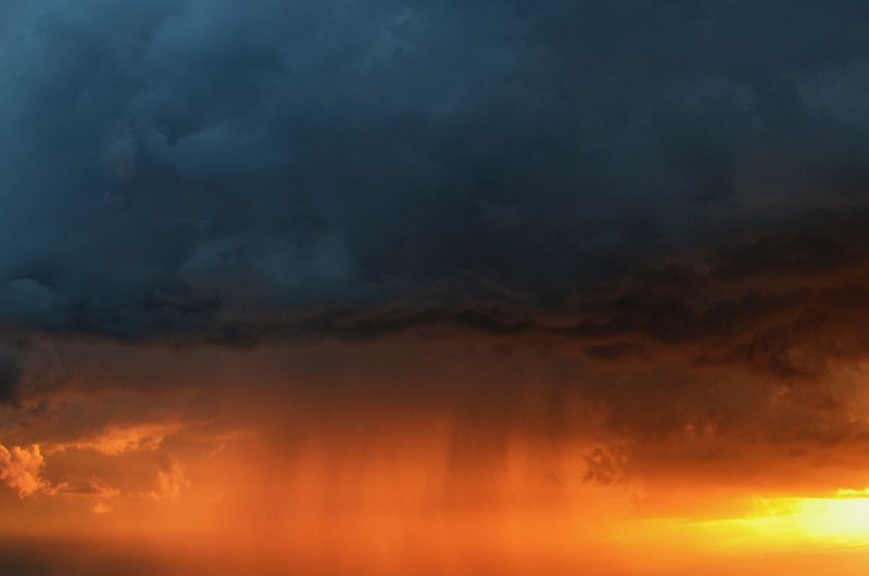 Vivid storm clouds with rain illuminated by a striking sunset sky.