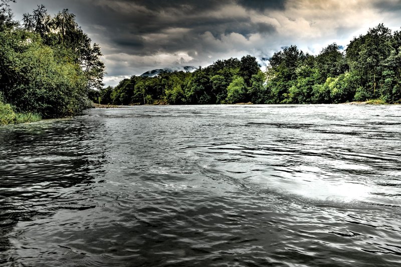 A scenic river view surrounded by lush trees under moody skies.