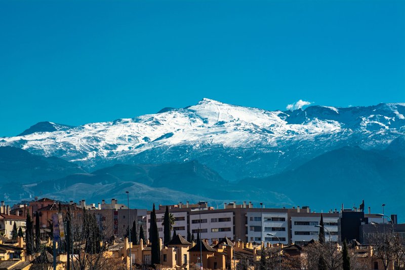 Panoramic view of snowy Sierra Nevada mountains towering over Granada's urban landscape.