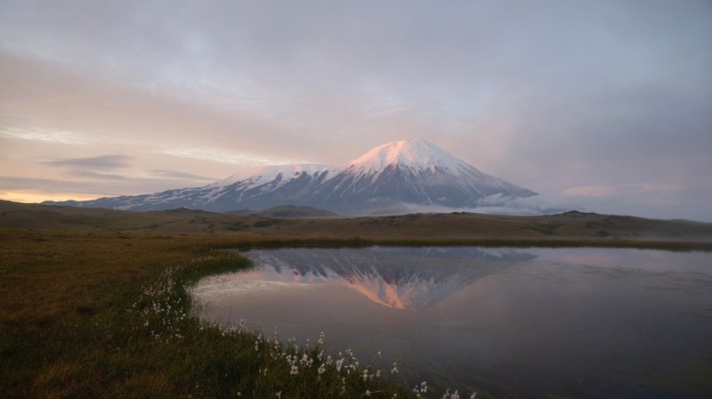 Stunning reflection of a snow-capped volcano in Kamchatka at dawn, surrounded by tranquil waters and a calm landscape.