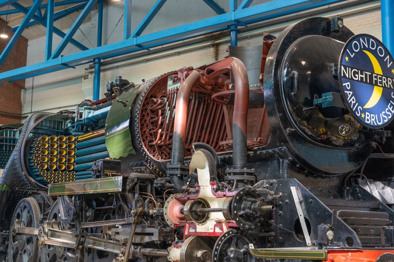 Intricate components of a vintage steam locomotive showcased indoors at a museum.