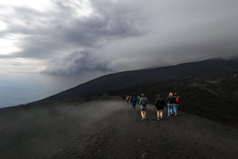Group of people hiking on a volcanic landscape under a dramatic cloudy sky, creating a moody atmosphere.