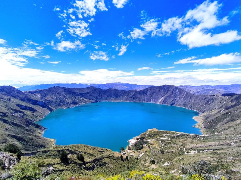 Stunning aerial view of Quilotoa Crater Lake surrounded by mountains under a vibrant blue sky.