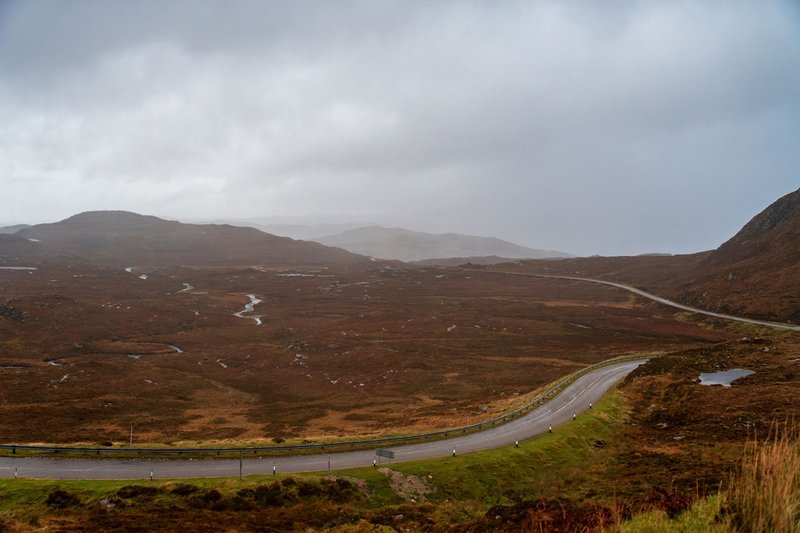 Sweeping view of a winding road through desolate highland terrain under a cloudy sky.