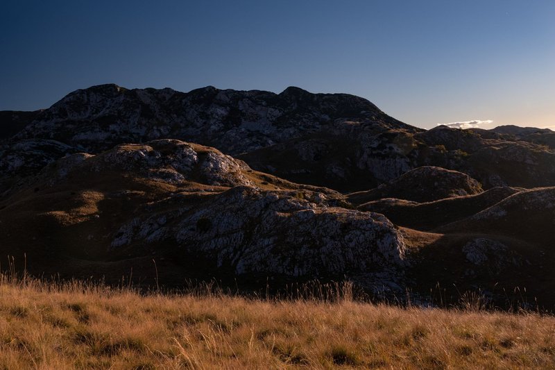 Serene rocky hill landscape with dry grass under a clear dusk sky.