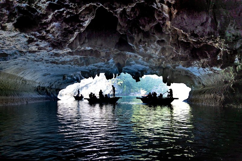 Silhouetted tourists in boats exploring a stunning water cave formation, showcasing natural beauty.