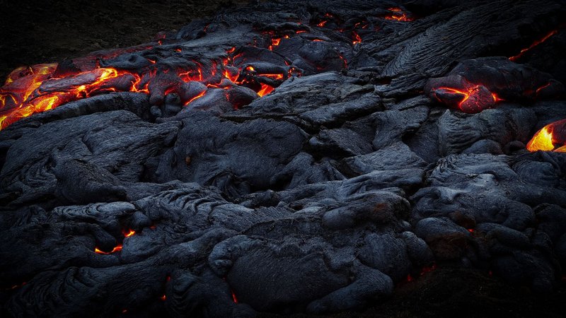 Close-up of glowing lava flowing over dark volcanic rock, showcasing intense heat and dramatic landscapes.