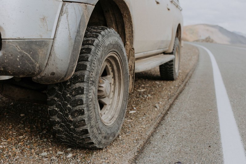 A rugged off-road vehicle's dirty tire on a gravel roadside in Altai Republic, Russia.