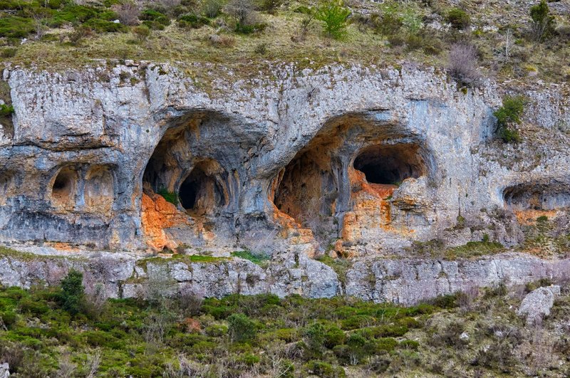 Explore intricate rock formations and natural caves carved into a rugged cliffside, showcasing geological wonders.