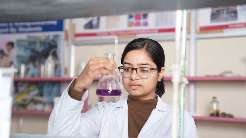 Female scientist examining a purple chemical solution in a laboratory setting.