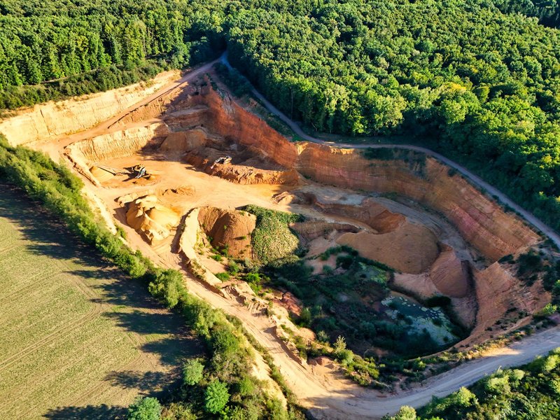 A stunning aerial shot of a large quarry contrasting sharply with lush green forests.
