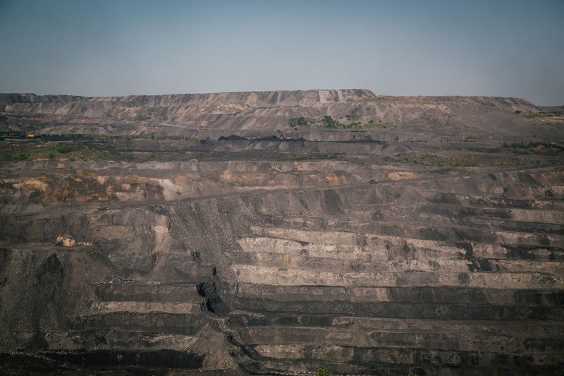 A vast open-pit coal mine under a clear blue sky, showcasing industrial landscape and natural rock formations.