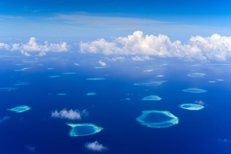 A stunning aerial shot capturing coral atolls in a vibrant blue sea under a cloudy sky.