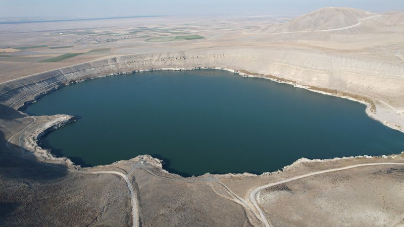 Drone shot of a barren crater lake surrounded by arid landscape in Turkey.