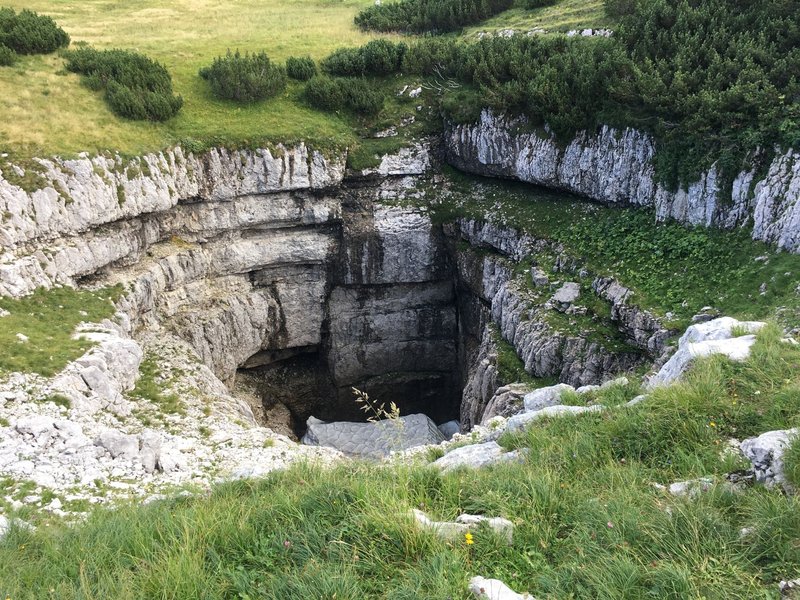Explore this dramatic limestone sinkhole surrounded by lush grass and rocky terrain.