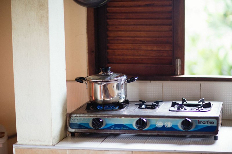 A stainless steel pot on a lit gas stove, next to a wooden shutter window.