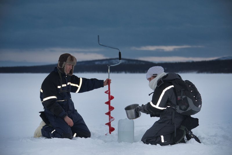 Two explorers use an ice auger on a frozen lake in Kiruna, Sweden during winter.