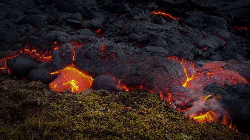 Intense lava flow exhibiting vibrant fiery hues and smoke.