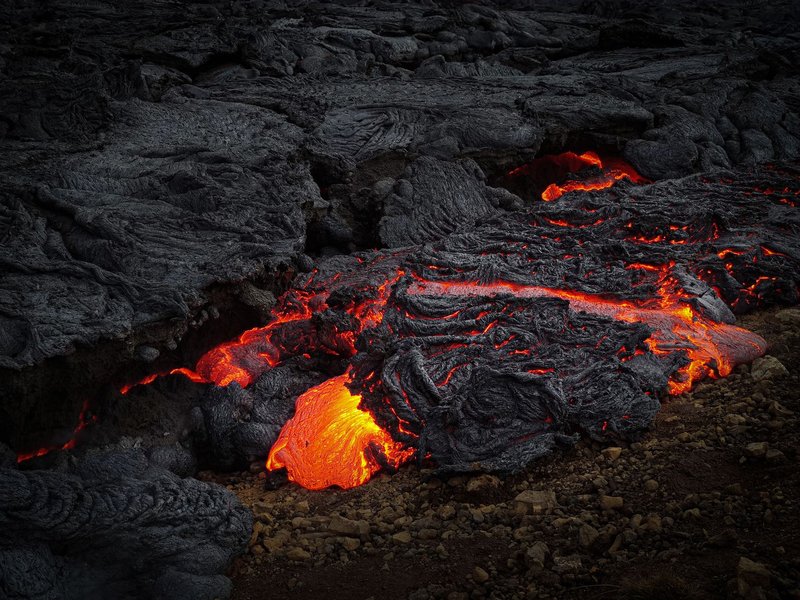 Molten lava flowing over hardened rock, showcasing volcanic activity and heat.