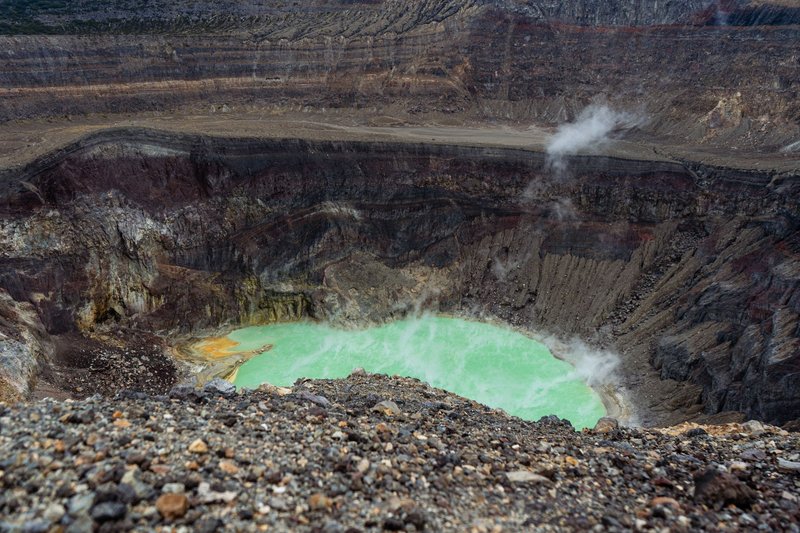 Panoramic view of an active volcano crater with steaming fumaroles and a striking turquoise lake.