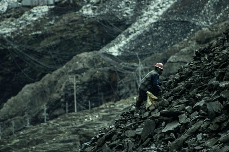 A solitary worker climbs a rocky slope in a barren quarry, wearing safety gear.