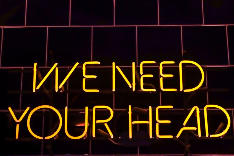 Vibrant neon sign 'WE NEED YOUR HEAD' glowing at night in Riga, Latvia.