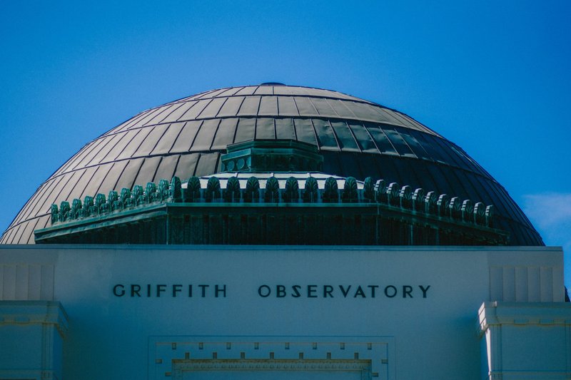 Close-up of Griffith Observatory's dome with 'Griffith Observatory' text under a clear blue sky.