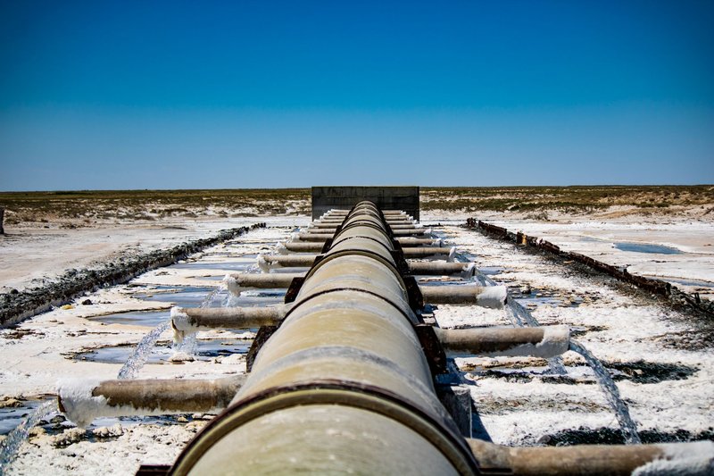 Large industrial pipeline discharging wastewater in arid, rural landscape under clear blue sky.