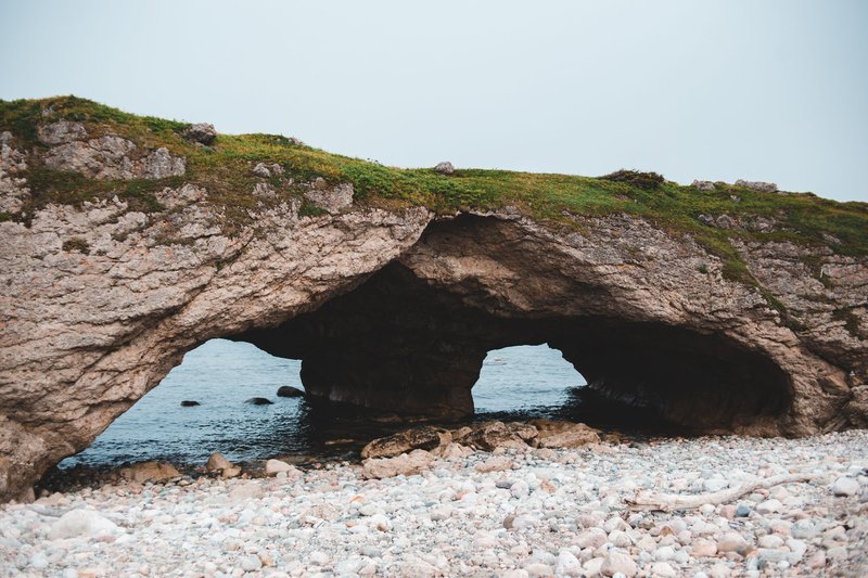 Rough formation of cliff archways on beach with white pebbles washed with peaceful waves