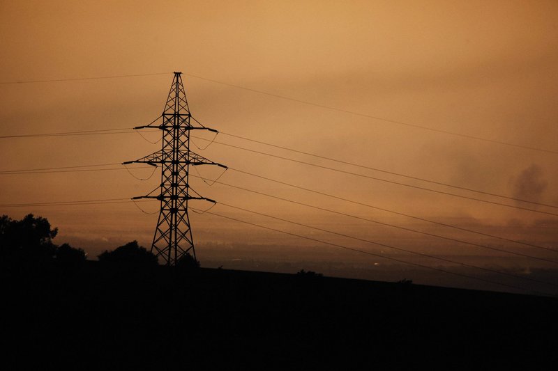 A power transmission tower silhouette against a warm sunset sky, symbolizing energy and infrastructure.